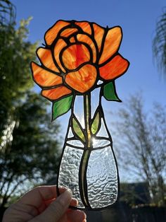 a hand holding up a stained glass flower in front of a blue sky and trees