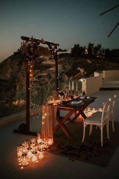 an outdoor dinner table with candles on the ground and lights in the air around it