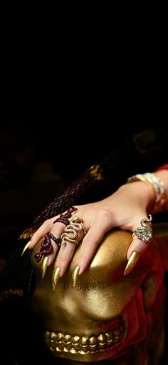 a woman's hand on top of a golden ball with rings and bracelets