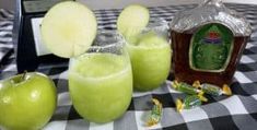 three glasses filled with green apple juice on top of a checkered table cloth next to an empty bottle