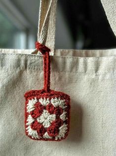 a red and white crocheted bag hanging from a hook on a string,