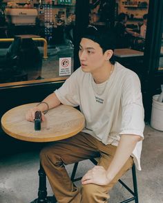 a young man sitting at a table in front of a store with his cell phone