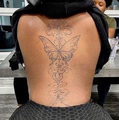 the back of a woman with a butterfly tattoo on her lower back, sitting at a table