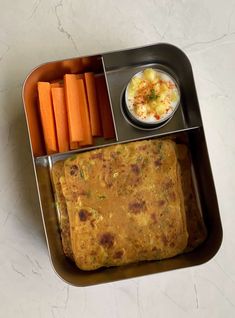 a metal container filled with food and carrots next to a small bowl of dip