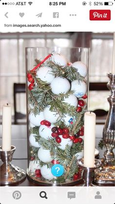 a glass vase filled with balls and greenery on top of a table next to candles