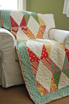 a couch with a quilt on it in front of a window and a white chair