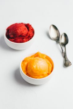 two bowls filled with ice cream next to spoons on a white counter top,