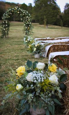 flowers and greenery are arranged in buckets on the grass near hay bales