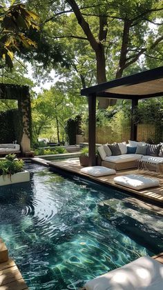 an outdoor living area with a pool and lounge furniture in the middle of it, surrounded by trees