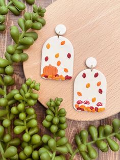 a pair of white and orange earrings sitting on top of a wooden table next to green leaves