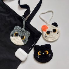 three crocheted cats are hanging from a black bag