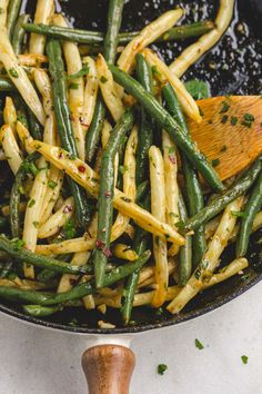 green beans and onions cooking in a pan with a wooden spatula on the side