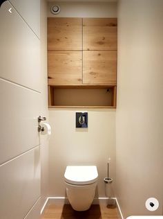 a white toilet sitting inside of a bathroom next to a wooden cabinet above it's door