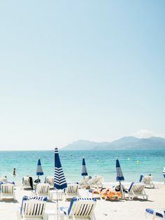 many chairs and umbrellas on the beach with people in the water behind them,