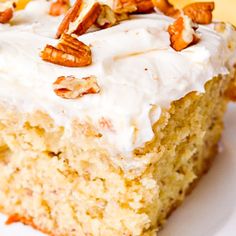 a piece of cake with white frosting and pecans on top is sitting on a plate