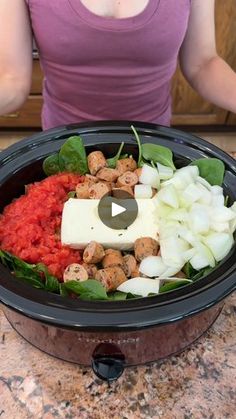 a woman standing in front of a slow cooker filled with vegetables and meats