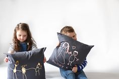 two children sitting on the floor with pillows that have drawings on them and one holding a pillow