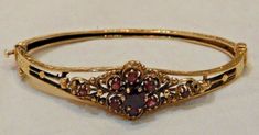 This is a wonderful vintage 14K yellow gold & ruby-red Garnet bangle bracelet The gold has wonderful ornate details along the sides and edges of the bracelet Along the middle of the bangle are the garnets which have intricate gold designs surrounding them The center garnet is the largest and has little garnets around it to resemble a flower The one side of the bangle has a clasp that allows the bracelet easy on and off access When opened, the gap measures about 2 1/4" The clasp is marked "14K" and some other maker's mark that we cannot make out The clasp works well & stays secure When clasped, the bracelet measures approx. 6" but it's difficult to get a true measurement since it's in an oval shape This bangle weighs 13.1 grams Gorgeous vintage bangle bracelet in very nice condition. Beauti Gold And Ruby Jewelry, Ornate Jeweled Gold Bracelet, Victorian Gold Bangle Bracelet With Intricate Design, Ornate Gold Ruby Jewelry, Victorian Gold Bracelet Collectible, Antique Art Deco Jewelry, Ornate Red Garnet Jewelry, Accesories Jewelry