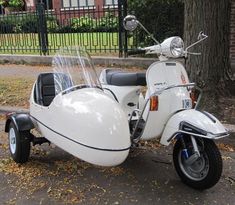 a white motor scooter parked on the side of the road next to a tree