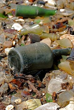 a bottle that is laying on some rocks and glass bottles are all around the ground