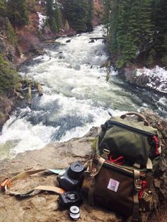 a backpack sitting on top of a rock next to a river with rapids in the background