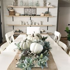 a dining room table with white pumpkins and greenery on the centerpiece, surrounded by shelves