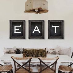 a dining room table with chairs and two framed eat signs on the wall above it