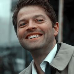 a close up of a person wearing a suit and tie with a smile on his face