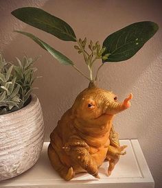 there is a fake dinosaur sitting next to a potted plant