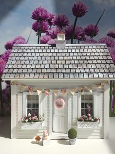 a doll house with purple flowers in the background