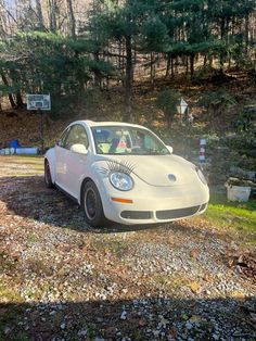 a white car parked on top of a gravel road in front of a wooded area