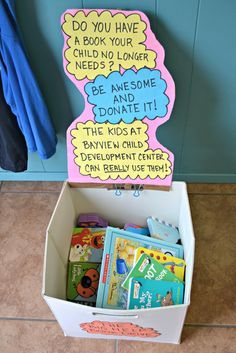 a cardboard box filled with children's books on the floor next to a coat rack