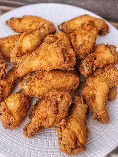 fried chicken pieces on a white plate sitting on a wooden table top, ready to be eaten