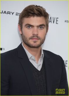 a man in a black suit and white shirt is looking at the camera with blue eyes