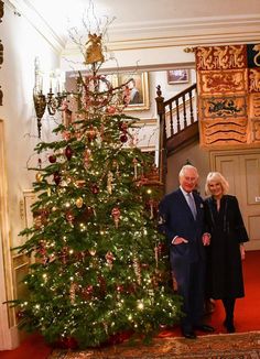 an older couple standing next to a christmas tree in a room with red carpeting