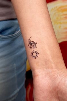 a woman's wrist with a small sun and moon tattoo on her left arm