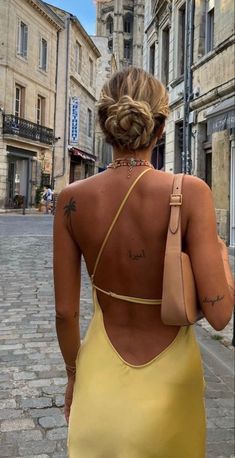 a woman in a yellow dress is walking down the street with her back to the camera