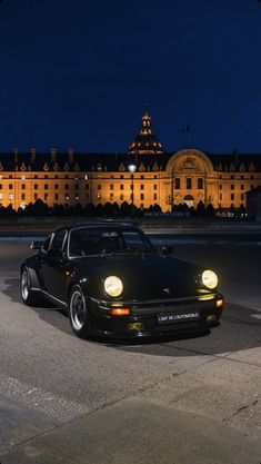 a black car parked in front of a large building at night with its lights on