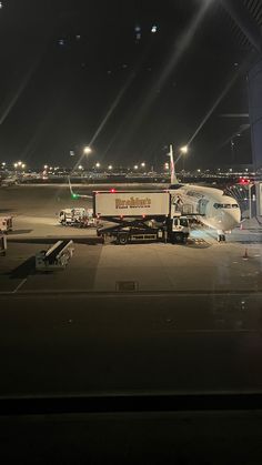 an airplane parked on the tarmac at night with its lights on and luggage being unloaded