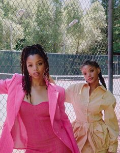 two women standing next to each other in front of a tennis court with trees behind them