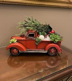 an old red truck with christmas decorations on the hood and windows is sitting on a table