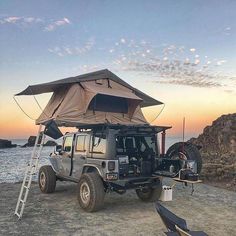 a jeep parked next to the ocean with an awning on it's roof