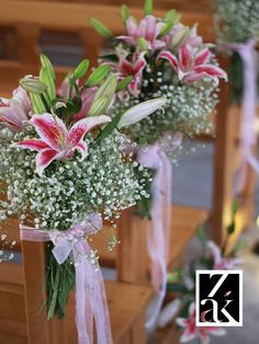 two vases filled with pink lilies and baby's breath sitting on top of wooden pews