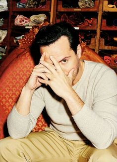 a man sitting on top of a red couch holding his hands to his face while looking at the camera