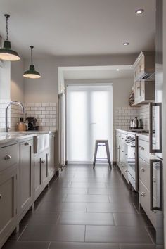 a long kitchen with white cabinets and stainless steel appliances on the counter top, along with an open door leading to another room