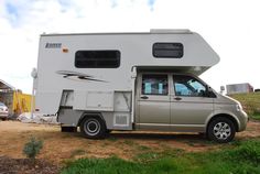 an rv parked on the side of a dirt road in front of a building and grass