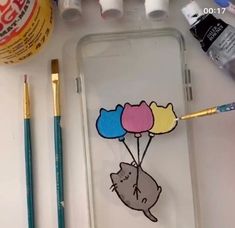 the phone case is decorated with three cats holding balloons and two paintbrushes next to it