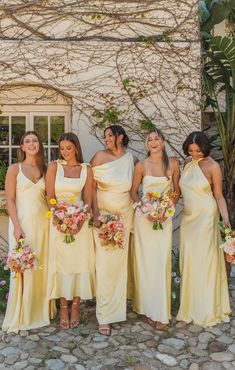 a group of women standing next to each other wearing yellow dresses and holding bouquets