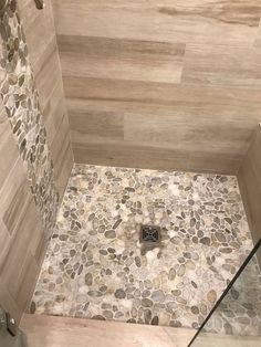 a walk in shower sitting next to a tiled wall and floor covered in pebbles on the ground