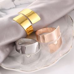 two gold and silver napkin rings sitting on top of a white plate next to an empty cup